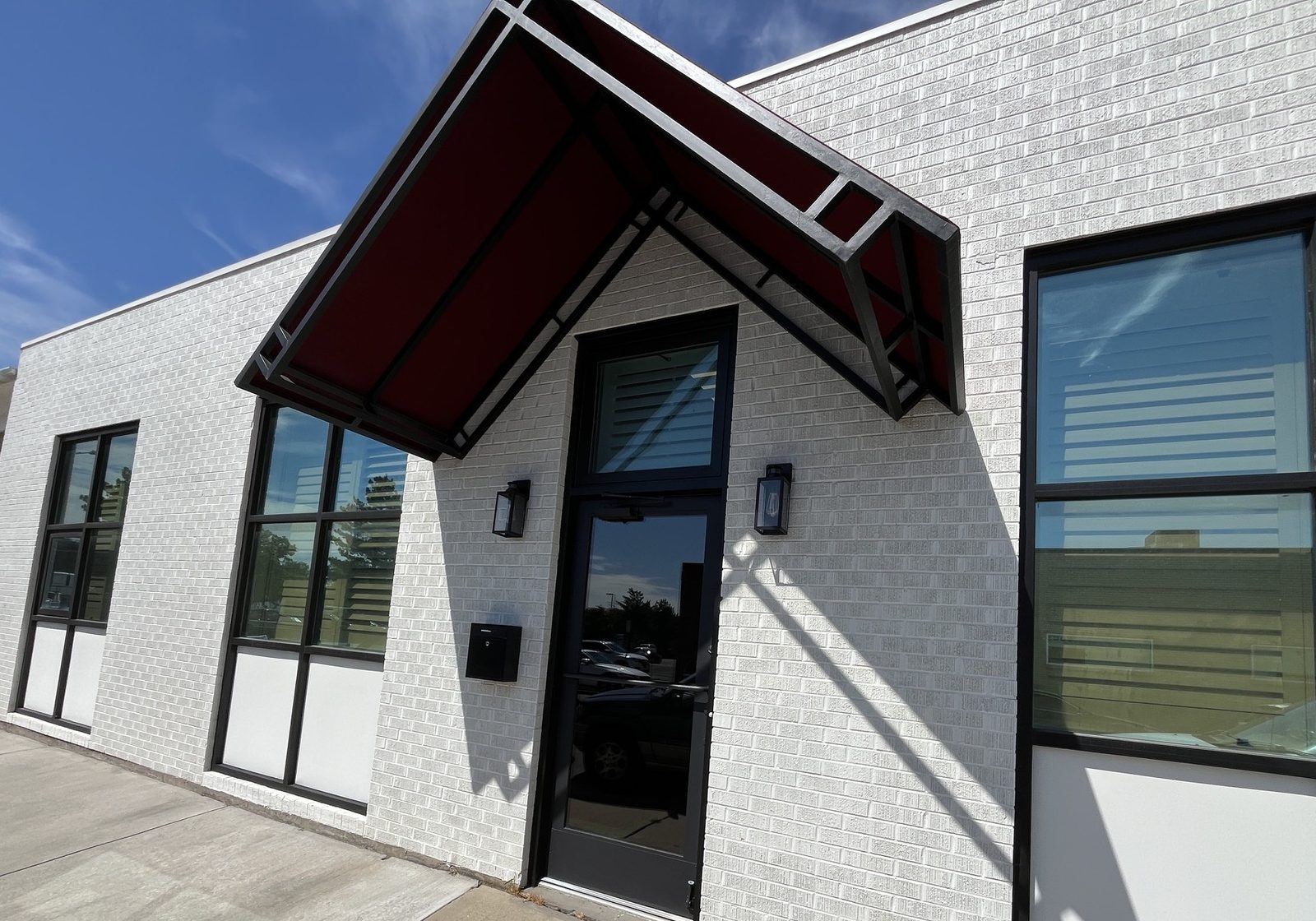 The entrance at 3989, a black glass door under a red steel awning set into white brick.